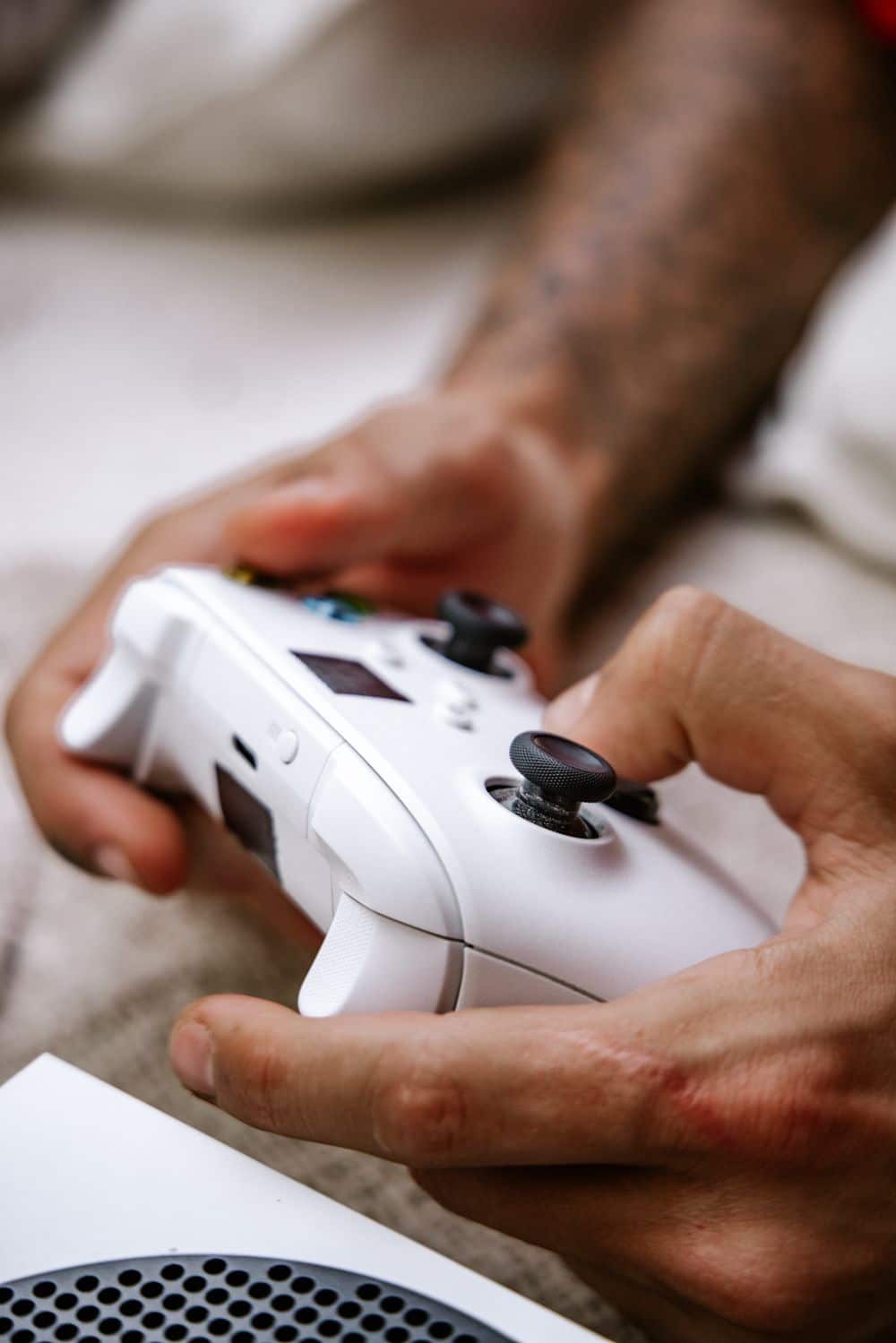Hands gripping a white gaming controller with a blurred background, showcasing a focus on gaming.