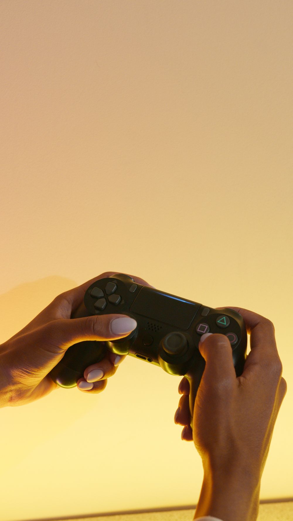 A close-up of hands holding a wireless game controller against a yellow background, capturing the gaming experience.